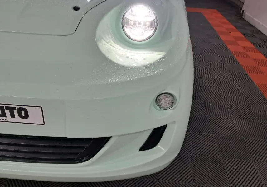 Gros plan sur l'avant droit vert d'une Aixam MINAUTO E chic 2025 avec phare allumé et antibrouillard visible.