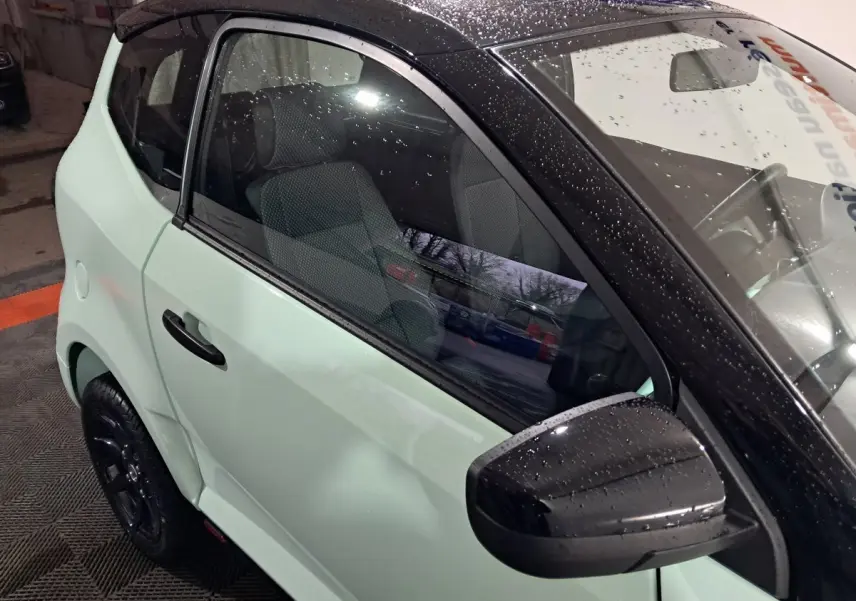 Vue côté conducteur d'une Aixam Minauto E chic 2025 vert clair avec toit noir et rétroviseur caméra.