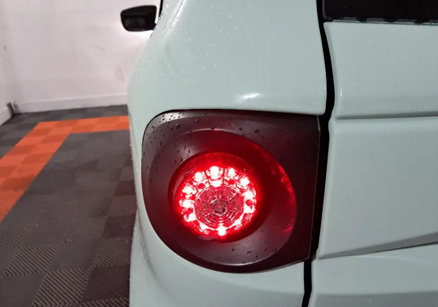 Gros plan sur le feu arrière droit rouge d'une Aixam Minauto E chic 2025 blanche avec gouttes d'eau.