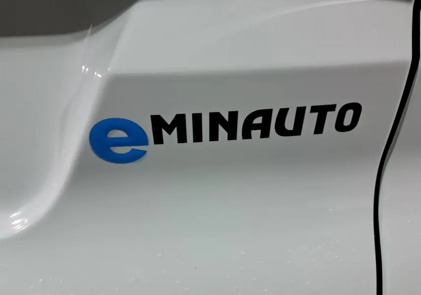 Gros plan sur le logo eMINAUTO en bleu et noir sur la carrosserie verte de l'AIXAM MINAUTO E chic côté conducteur.