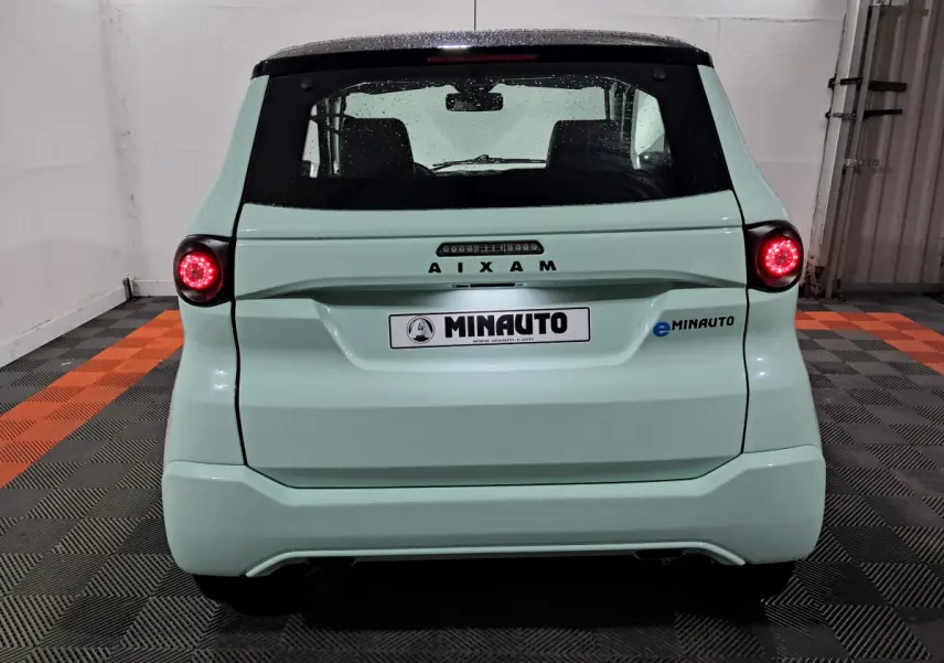 Vue arrière d'une AIXAM MINAUTO E chic 2025 verte avec feux ronds allumés et logo eMINAUTO visible à droite.