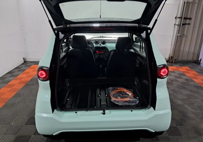 Vue arrière d'une Aixam MINAUTO E chic 2025 verte avec coffre ouvert et câble de recharge visible à l'intérieur.