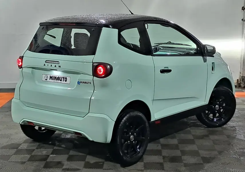 Vue 3/4 arrière droite d'une Aixam MINAUTO E chic électrique vert clair avec jantes noires et caméra sur le côté conducteur.