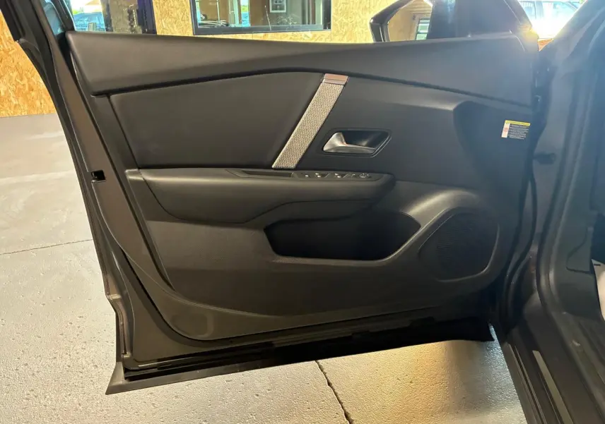 Vue intérieure de la porte avant gauche d'une Citroën C4 X gris 2024, avec garniture noire et commandes électriques.