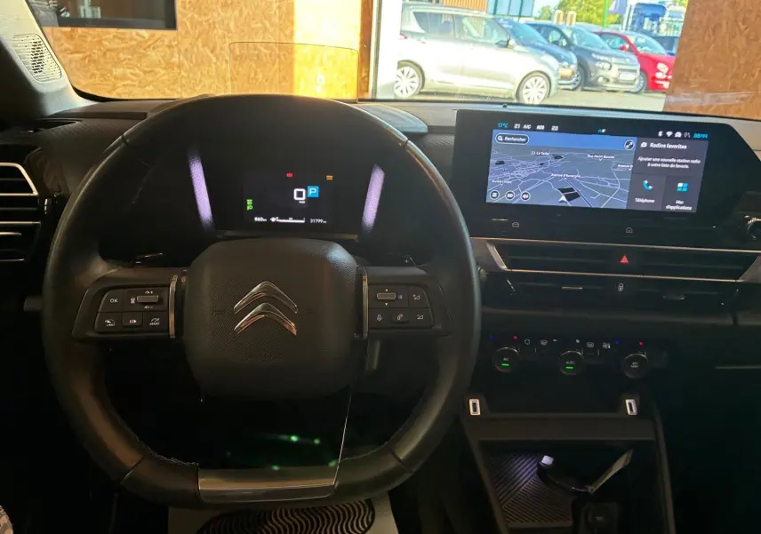 Vue intérieure centrée sur le volant et le tableau de bord numérique du Citroën C4 X gris 2024 avec écran tactile GPS.