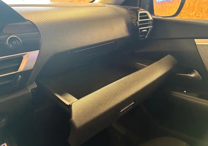 Vue intérieure côté passager du coffre à gants ouvert du Citroën C4 X gris 2024, soulignant la texture du tableau de bord.
