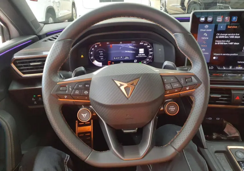 Vue intérieure centrée sur le volant cuir perforé CUPRA avec tableau de bord digital et écran tactile à droite.