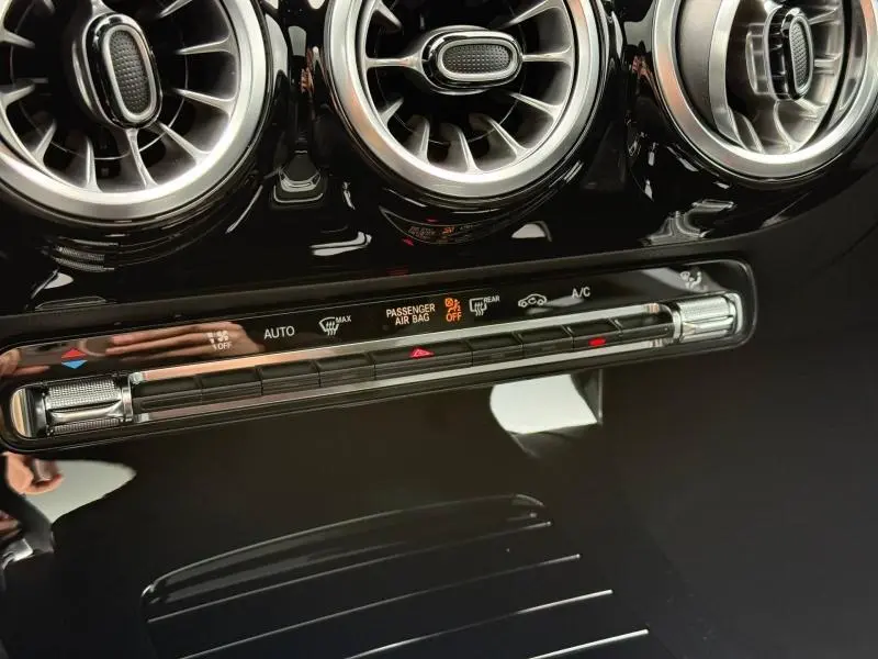 Détail du tableau de bord noir brillant de la Mercedes Classe A 200 d AMG Line, avec aérateurs ronds chromés et commandes climatisation.