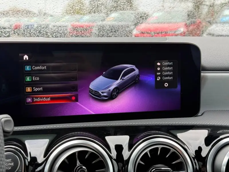 Écran tactile intérieur montrant la Mercedes Classe A gris montagne en vue 3/4 avant avec modes de conduite sélectionnables.