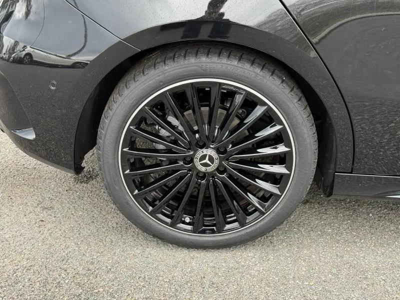 Gros plan sur la roue arrière gauche noire brillante avec jante AMG au design étoilé du Mercedes Classe A gris montagne métallisé.