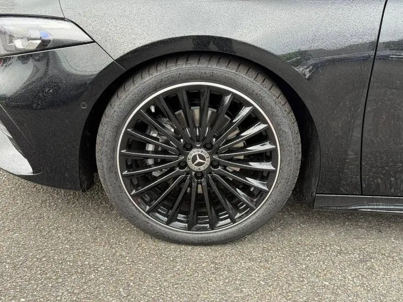 Gros plan sur la roue avant gauche noire à jantes alu noires brillantes d'une Mercedes Classe A gris montagne métallisé.