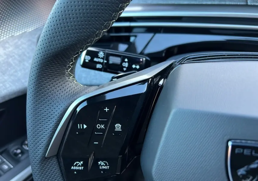 Gros plan sur le volant cuir perforé du Peugeot 3008 Hybrid 145 GT, avec commandes multifonctions et tableau de bord noir brillant.
