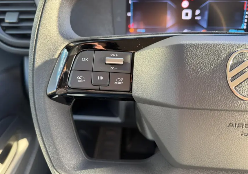 Gros plan sur les commandes à gauche du volant gris du Citroën Jumpy XL 2025 avec écran numérique en arrière-plan.