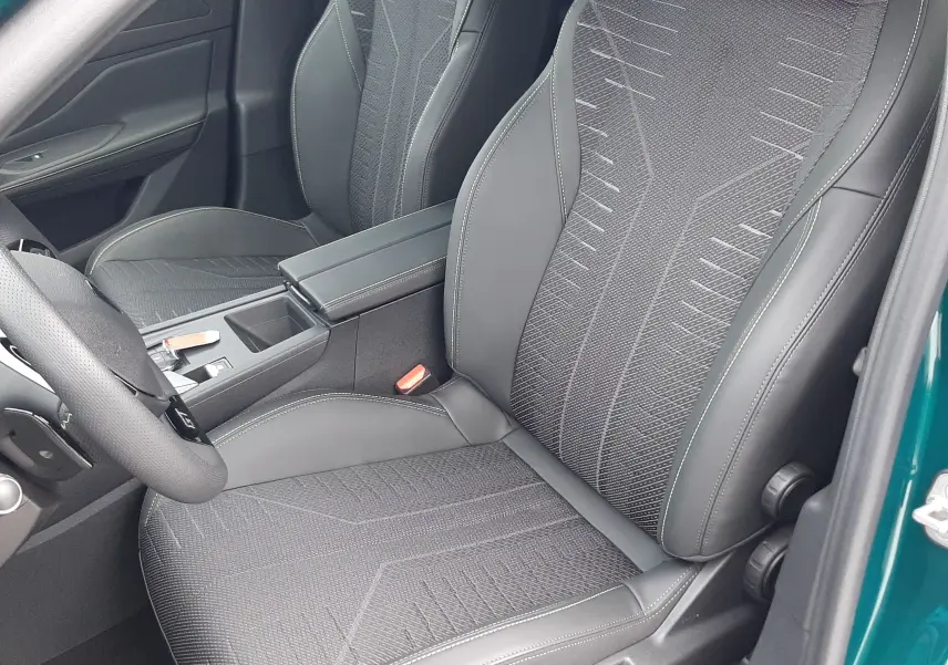 Vue intérieure côté conducteur de la Peugeot 308 2025 bleu Lagoa, sièges noirs avec surpiqûres et console centrale visible.