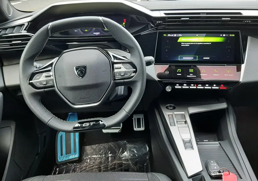 Vue intérieure frontale du poste de conduite de la Peugeot 308 GT hybride 2025 avec volant compact et écran tactile central.