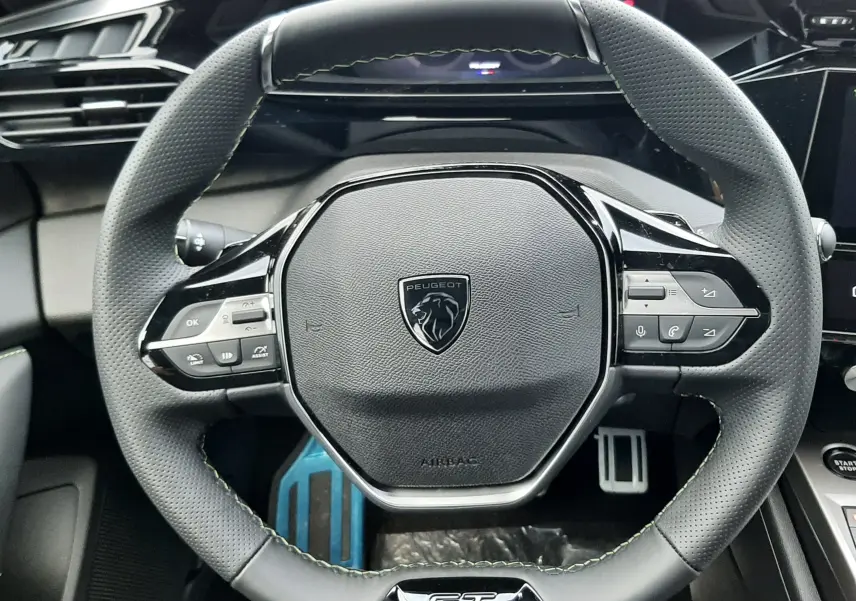 Vue rapprochée du volant noir GT avec logo Peugeot au centre dans l'habitacle d'une 308 Bleu Lagoa 2025.