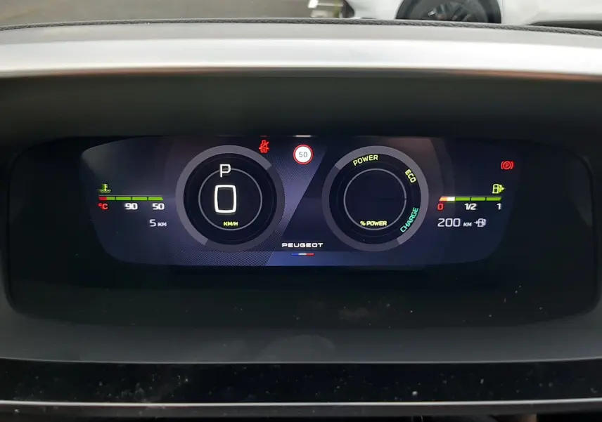 Tableau de bord numérique de Peugeot 308 hybride 2025 affichant vitesse à zéro et indicateurs de puissance et autonomie.