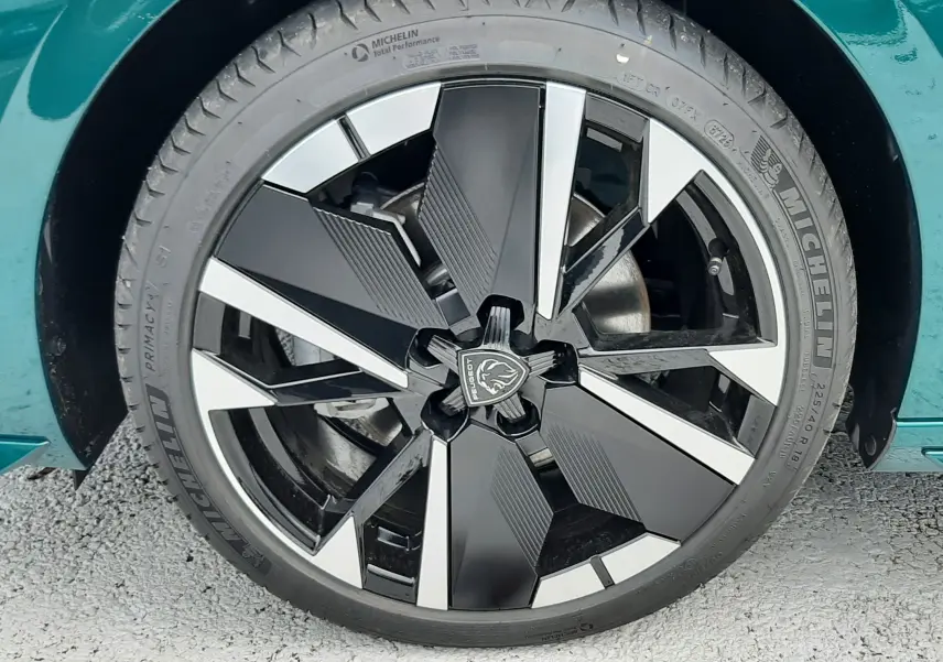 Gros plan sur la jante noire et argentée d'une Peugeot 308 Bleu Lagoa, soulignant le design moderne et le pneu Michelin.