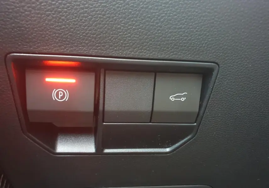 Boutons de commande du frein de parking électrique et ouverture du coffre sur tableau de bord noir d'une Dacia Bigster.