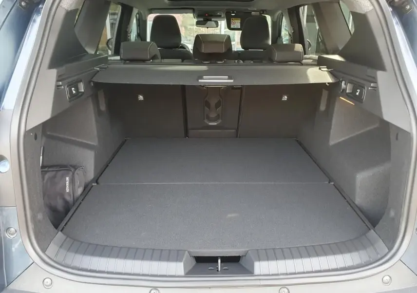 Coffre ouvert vu de l'arrière du Dacia Bigster bleu indigo avec banquette arrière et toit panoramique visibles.