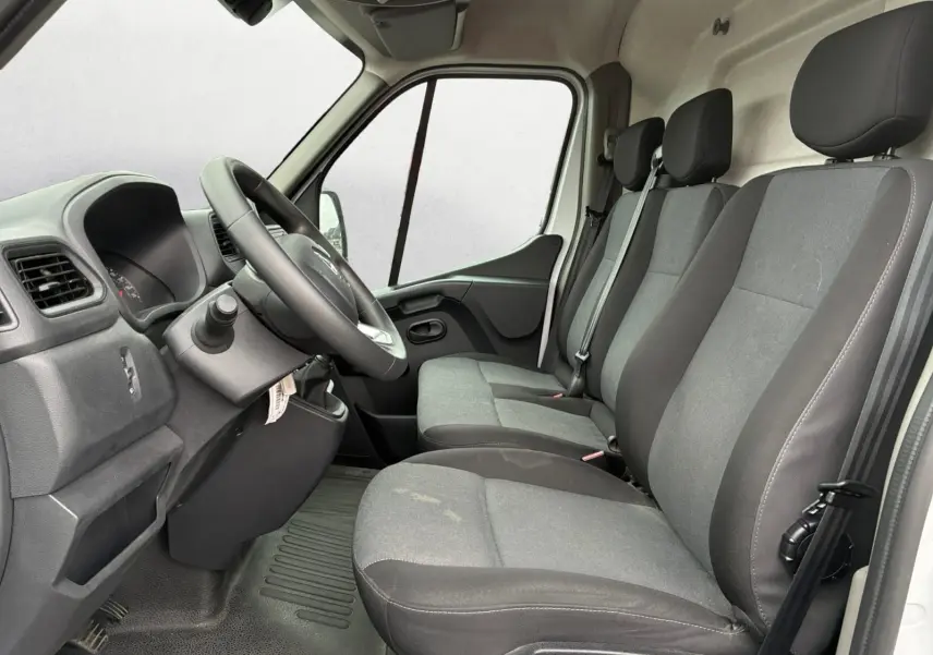 Vue intérieure côté conducteur du Renault Master 2024 blanc, montrant les trois sièges avant gris et le tableau de bord simple.