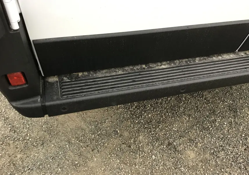 Gros plan sur la marche latérale noire du Peugeot Boxer Fourgon blanc, côté gauche, avec traces de boue.