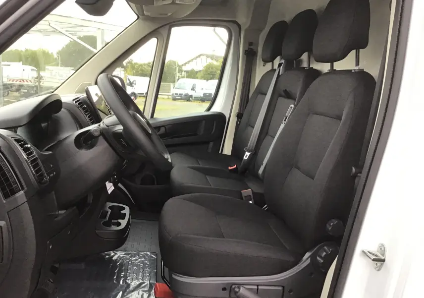 Intérieur du Peugeot Boxer Fourgon blanc 2025, vue côté conducteur sur les trois sièges noirs et le tableau de bord.