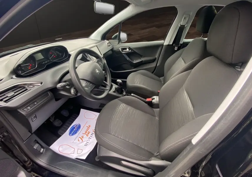 Intérieur avant droit d'une Peugeot 208 Affaire noire 2019, sièges tissu noir et tableau de bord avec volant compact.