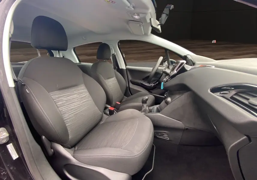 Vue intérieure côté conducteur de la Peugeot 208 Affaire noire, sièges tissu noir et tableau de bord moderne.