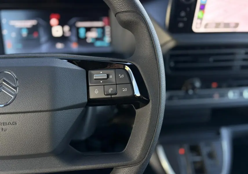 Gros plan sur le volant noir du Citroën Jumpy 2025, avec commandes audio et écran tactile flou en arrière-plan.