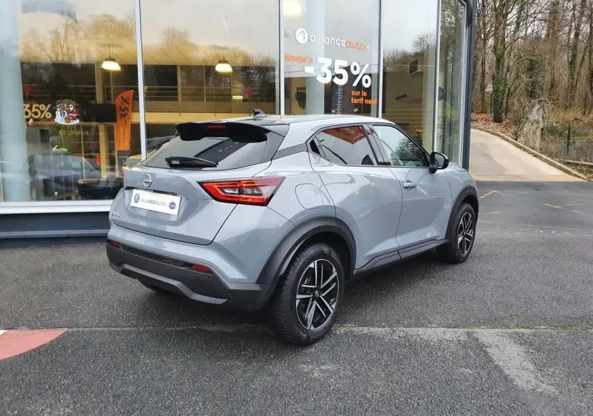 Nissan Juke gris céramique vu en 3/4 arrière droit, avec jantes alliage 17'' et antenne aileron de requin noire.