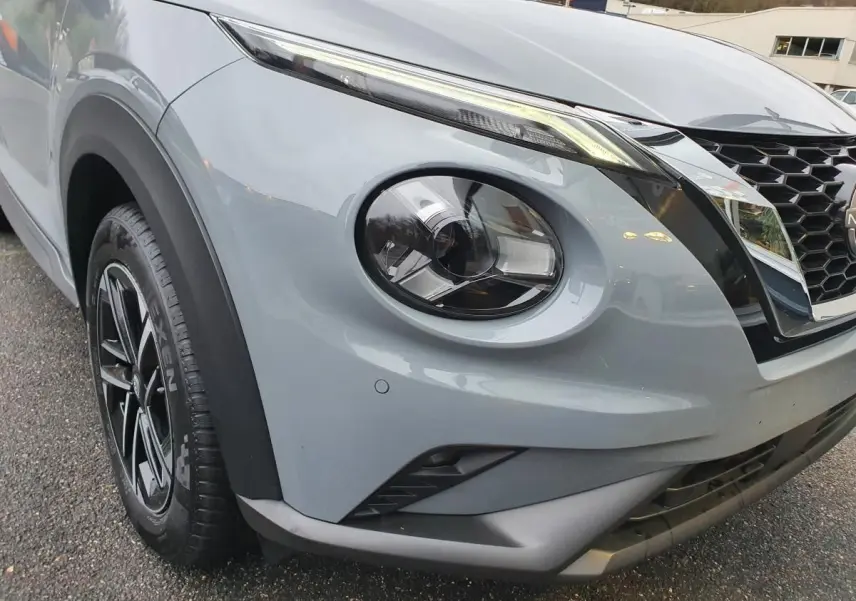 Gros plan sur l'avant droit gris céramique du Nissan Juke 2025 avec phares ronds et calandre en nid d'abeille.