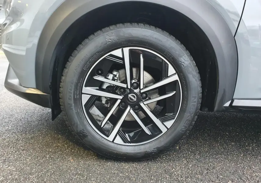 Gros plan sur la roue avant gauche du Nissan Juke gris céramique avec jante alliage noire et argentée.