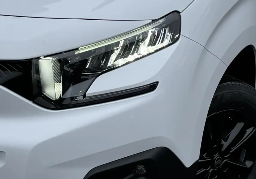 Gros plan sur le phare avant droit et la jante alliage noire du Citroën Berlingo Multispace blanc Glacier 2025.