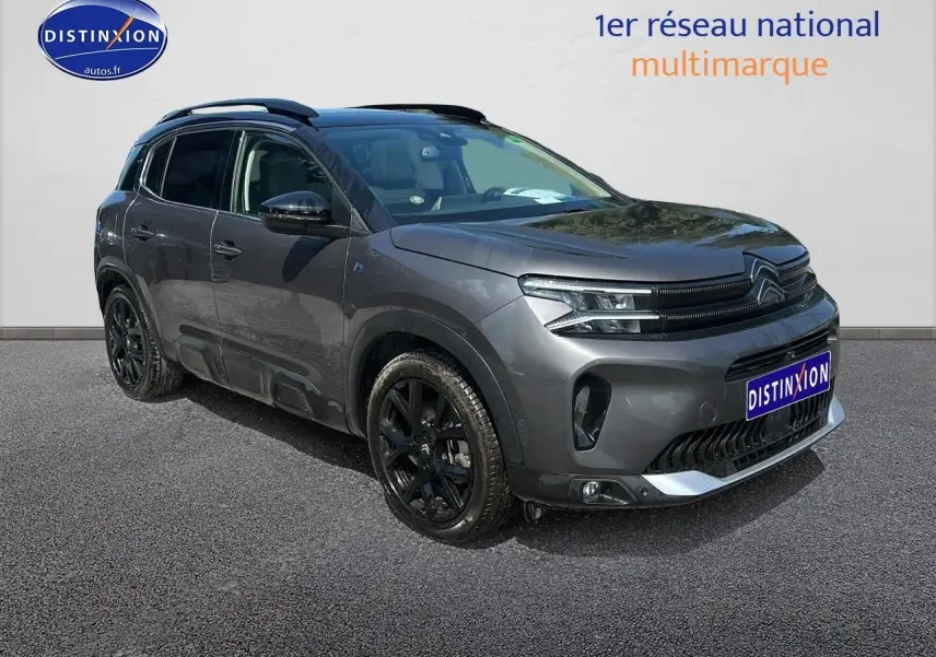 Vue 3/4 avant droit du Citroën C5 Aircross gris platinium avec jantes noires et barres de toit visibles.