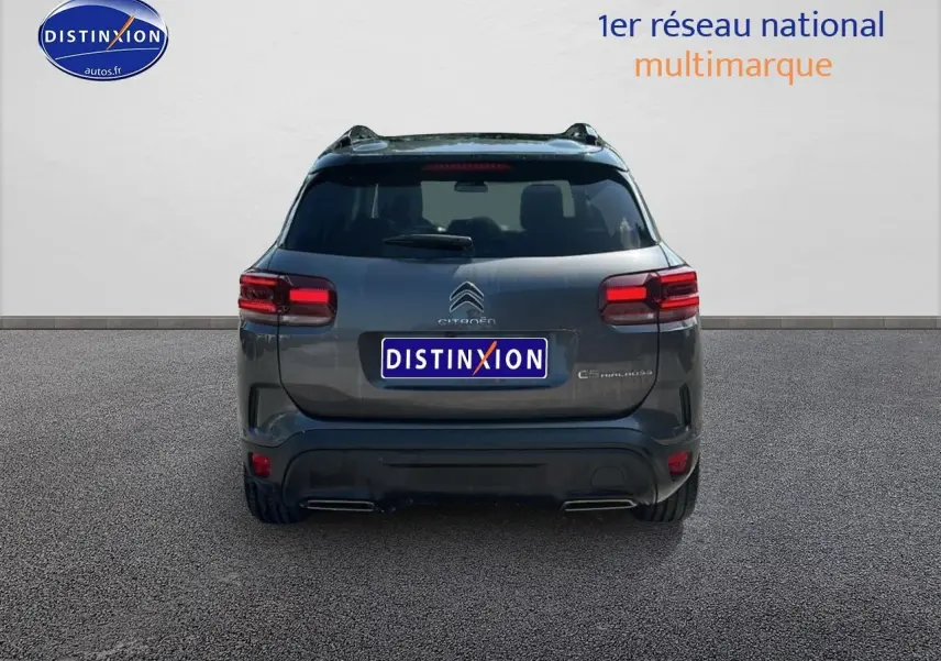 Vue arrière d'un Citroën C5 Aircross gris platinium avec feux arrière LED et barres de toit visibles.