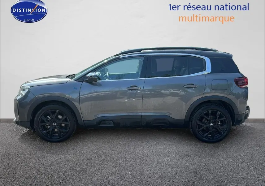 Vue de profil côté gauche d’un Citroën C5 Aircross gris platinium avec jantes noires et barres de toit.