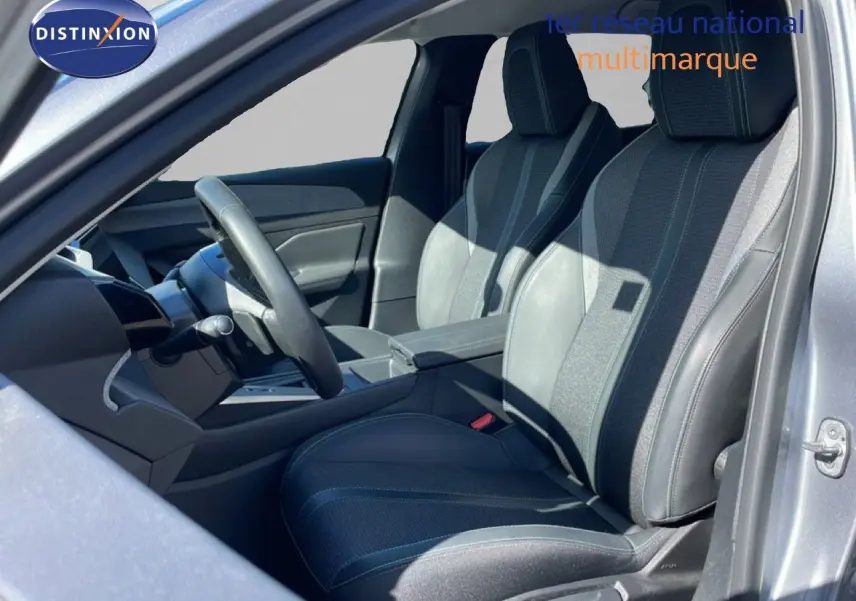 Vue intérieure côté conducteur de la Peugeot 308 SW Hybrid 2025, sièges gris noir en tissu et cuir, volant multifonction.