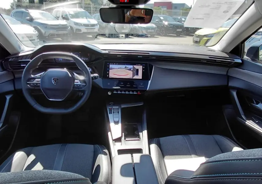 Vue intérieure avant de la Peugeot 308 Hybrid 145 gris, avec volant compact et écran tactile affichant la caméra de recul.