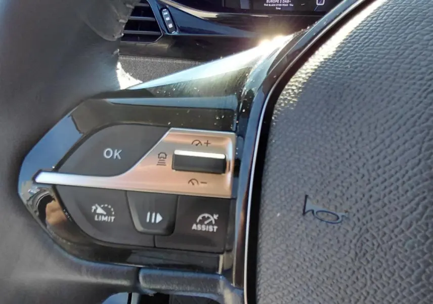 Détail du volant côté gauche du Peugeot 308 Hybrid gris, montrant les commandes de régulateur et limiteur de vitesse.