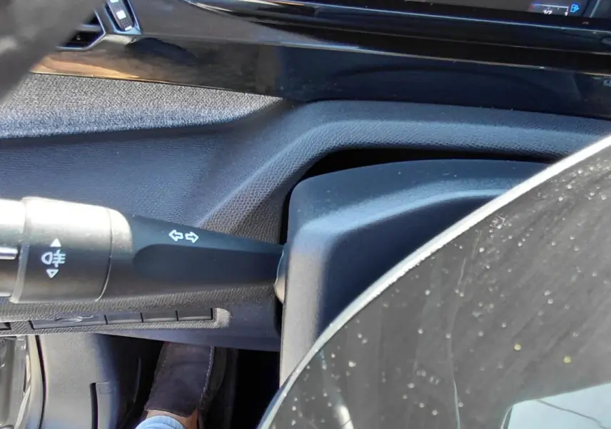 Détail de la commande des feux et clignotants côté gauche du volant dans l’habitacle d’une Peugeot 308 Hybrid 145 gris.