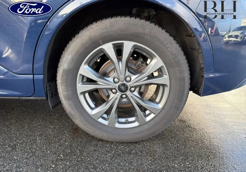 Gros plan sur la roue avant gauche et la jante alu grise d’un Ford Kuga bleu Abysse 2023.