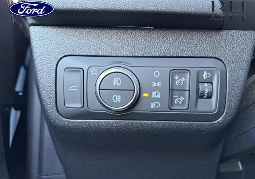 Gros plan sur les commandes d’éclairage et de réglage des phares du Ford Kuga 2023, tableau de bord noir.