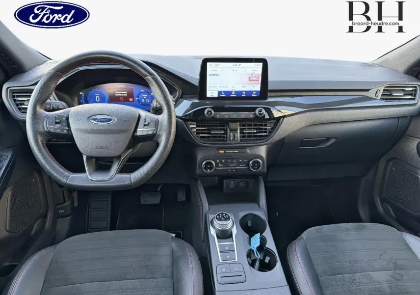 Vue intérieure avant du Ford Kuga 2023, tableau de bord noir avec écran tactile central et volant cuir multifonction.