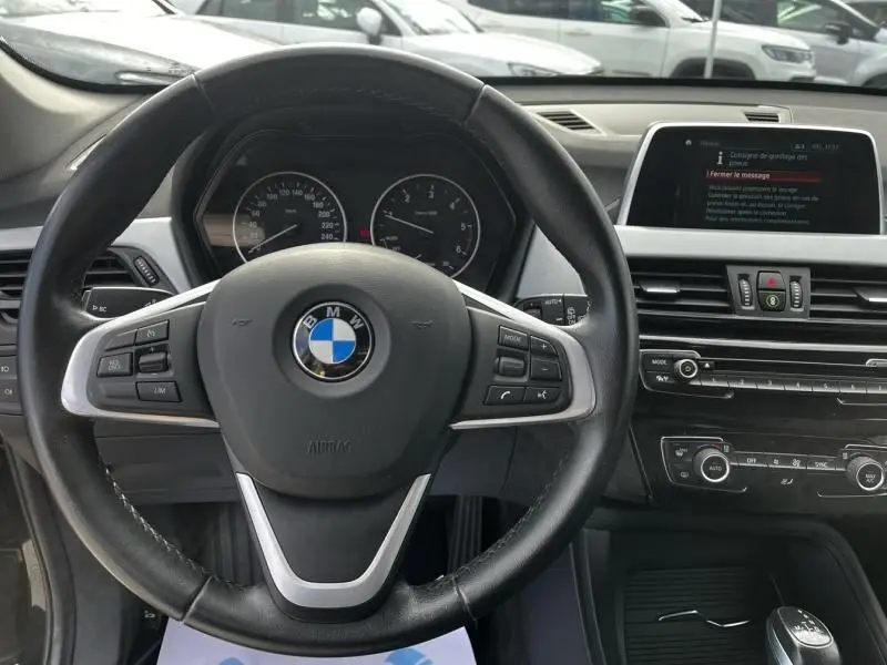 Vue intérieure centrée sur le volant cuir noir et le tableau de bord du BMW X1 20D 2017, avec écran multimédia visible.