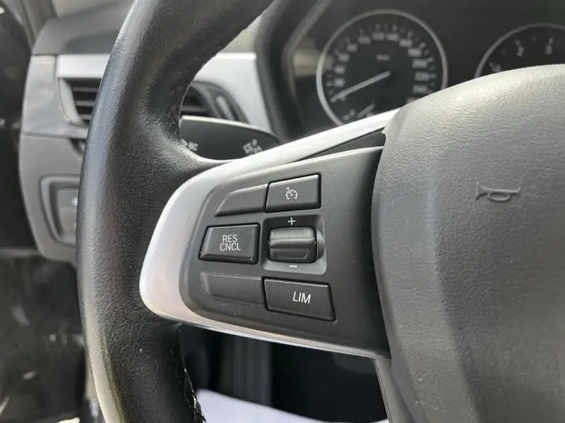 Gros plan sur les commandes de régulateur de vitesse au volant noir du BMW X1 20D 2017, côté gauche.