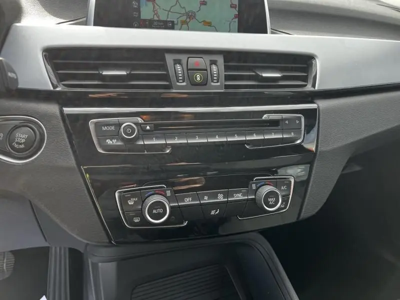Vue rapprochée du tableau de bord noir brillant du BMW X1 20D 2017, avec commandes climatisation et écran GPS intégré.