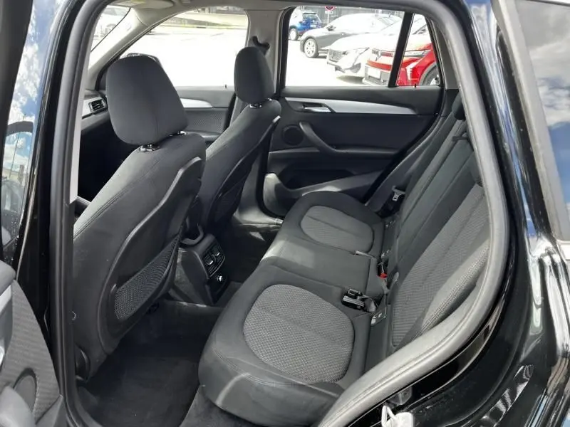 Vue intérieure arrière côté droit du BMW X1 noir métal 2017, sièges tissu noir avec appuie-têtes et aérateurs centraux visibles.