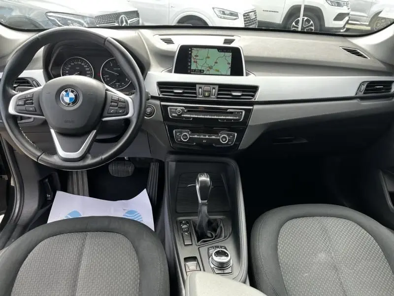 Vue intérieure avant du BMW X1 noir métal 2017, montrant le volant, la console centrale avec écran GPS et la boîte automatique.