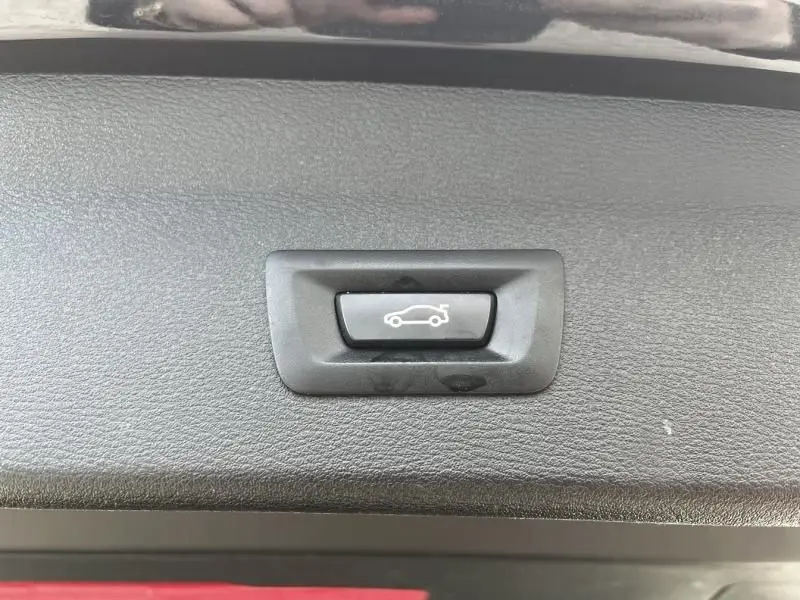 Bouton d'ouverture électrique du coffre sur un BMW X1 20D noir métal, vue rapprochée intérieure.